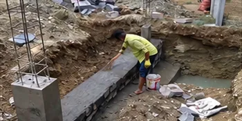 Worker levelling a plinth beam next to a cast column